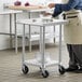 A person in an apron pouring liquid into a bowl on a Regency stainless steel work table with casters.