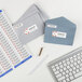 A white table with a keyboard, pen, and envelopes with Avery Sure Feed Return Address Labels on them.