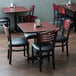 A Lancaster Table & Seating dining set with mahogany chairs and padded seats at a table with a reversible cherry and black top.