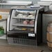 An Avantco black curved glass refrigerated deli case on a counter with meat inside.