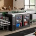 An Avantco black counter height back bar refrigerator with drinks on the counter.