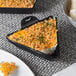 A Lodge mini cast iron triangular server with cheese and crackers on it.