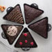 A Lodge triangle shaped brownie pan with four brownies topped with ice cream and chocolate sauce.