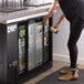 A woman putting a bottle in a Avantco back bar refrigerator.