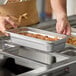 A person holding a Choice stainless steel steam table pan full of food.