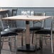 A Lancaster Table & Seating solid wood live edge table with antique white wash finish on a table with black chairs.