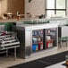 An Avantco stainless steel back bar refrigerator on a counter with bottles inside.