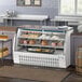 An Avantco white curved glass refrigerated deli case on a counter displaying meat and cheese.