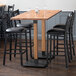 A Lancaster Table & Seating live edge wood bar table with black chairs around it.