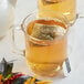 A glass mug of Numi Organic Decaf Ginger Lemon tea with a tea bag of herbs in it.