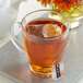 A close-up of a glass cup of Numi Organic Rooibos tea with a tea bag in it.
