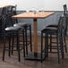 A Lancaster Table & Seating bar table with a wooden live edge top and a black metal base.