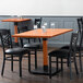 A Lancaster Table & Seating solid wood live edge table with a rustic mahogany finish and chairs with glasses on top.