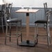 A Lancaster Table & Seating antique white wash wooden bar height table base with two black leather bar stools.