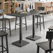A Lancaster Table & Seating industrial live edge bar height table with a slate gray finish and chairs in a room.