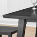 A Lancaster Table & Seating square solid wood bar height table in antique slate gray with a wine glass on it.