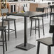 A Lancaster Table & Seating live edge bar height table with a slate gray finish and black stools on either side.