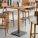 A Lancaster Table & Seating solid wood live edge bar height table with a honey maple finish and four stools in a room.