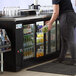 A woman standing in front of a black Avantco back bar refrigerator with glass doors.