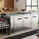 A stainless steel counter height refrigerator with bottles on a metal shelf.