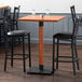 A Lancaster Table & Seating live edge bar height table with two chairs around it.