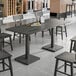 A Lancaster Table & Seating live edge wood table with a slate gray finish and black chairs.