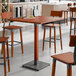 A Lancaster Table & Seating bar height table with a rustic mahogany finish and wooden legs with four stools at it.