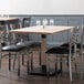 A Lancaster Table & Seating solid wood live edge dining table with antique white wash finish and chairs with black cushions around it.