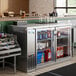 An Avantco back bar refrigerator with bottles on metal shelves.