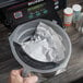 A hand placing a Numi Classic Black Iced Tea filter bag into a grey container.