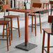 A bar height table with a rustic mahogany finish and industrial metal accents.