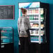 A woman standing in front of a black Avantco refrigerated air curtain display case.