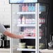 A man standing in front of an Avantco refrigerated air curtain merchandiser filled with drinks.