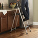 A woman standing on a Cosco platinum and black step stool with a handrail.