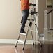 A man standing on a Cosco aluminum step ladder with a work platform.