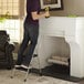 A man standing on a Cosco 2 step ladder using a drill.