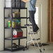 A man standing on a Cosco aluminum 3-step ladder placing buckets on a shelf.