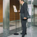 A man in a suit holding a briefcase standing next to a Durable Sherpa Infobase sign stand.