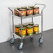 A Regency two-shelf stainless steel utility cart full of canned food.