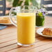 A Libbey plastic pitcher of orange juice on a table next to a plate of food.