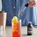 A person pouring Old Forester Hummingbird Rose and Citrus Bitters into a glass of liquid.