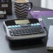 A DYMO label maker on a desk next to a notebook.