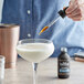 A hand using a dropper to pour Old Forester Bohemian Spiced Cherry and Chocolate Bitters into a cocktail glass.