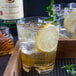 A Libbey plastic double rocks glass with a drink, ice, and a lemon slice.