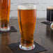 A Libbey Tritan plastic Pilsner glass of beer on a table with a napkin.