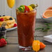 A Libbey Tritan plastic stackable cooler glass filled with a drink with ice and a yellow and orange pepper next to a plate of food.