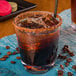 A Libbey Tritan plastic rocks glass with brown liquid, ice, and a straw.