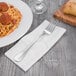 Oneida Baguette 18/10 stainless steel table fork on a napkin next to a plate of spaghetti.