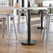 A Lancaster Table & Seating black cast iron column table base with stools and a cup on it.