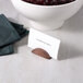 An American Metalcraft hammered copper half moon table card holder holding a name card on a table with a bowl of food.